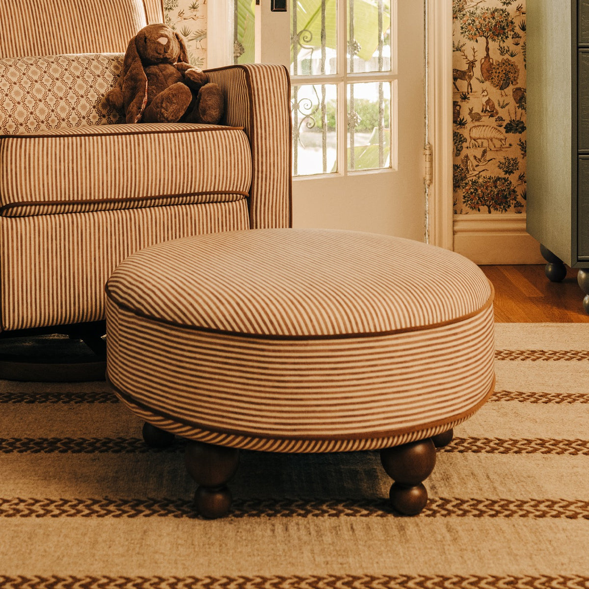 Babyletto round striped ottoman with wooden ball feet in a nursery