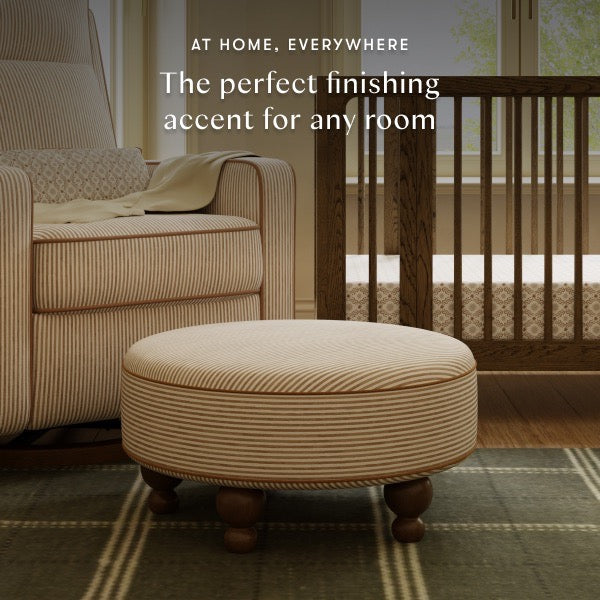 Babyletto round striped ottoman in a nursery with a matching armchair and wooden crib