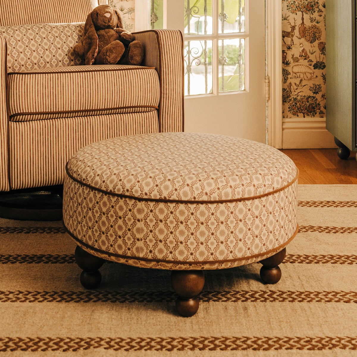 Babyletto round patterned ottoman with wooden bun feet on a striped rug