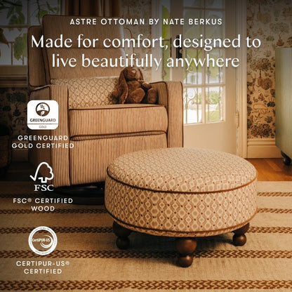 Babyletto Astre ottoman with patterned fabric and wooden feet in a room with a striped armchair