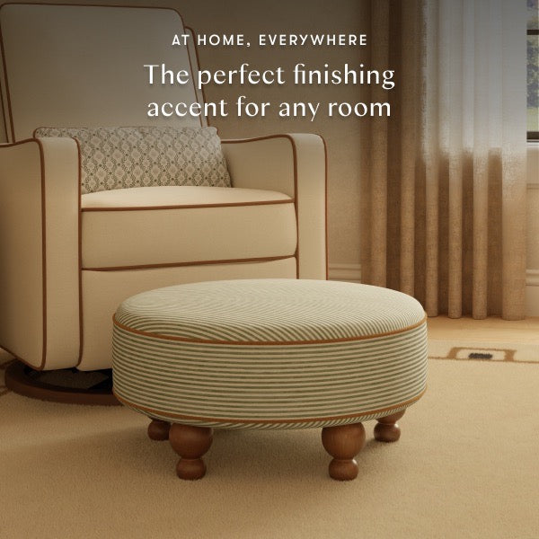 Babyletto round striped ottoman with wooden feet in front of a cream armchair