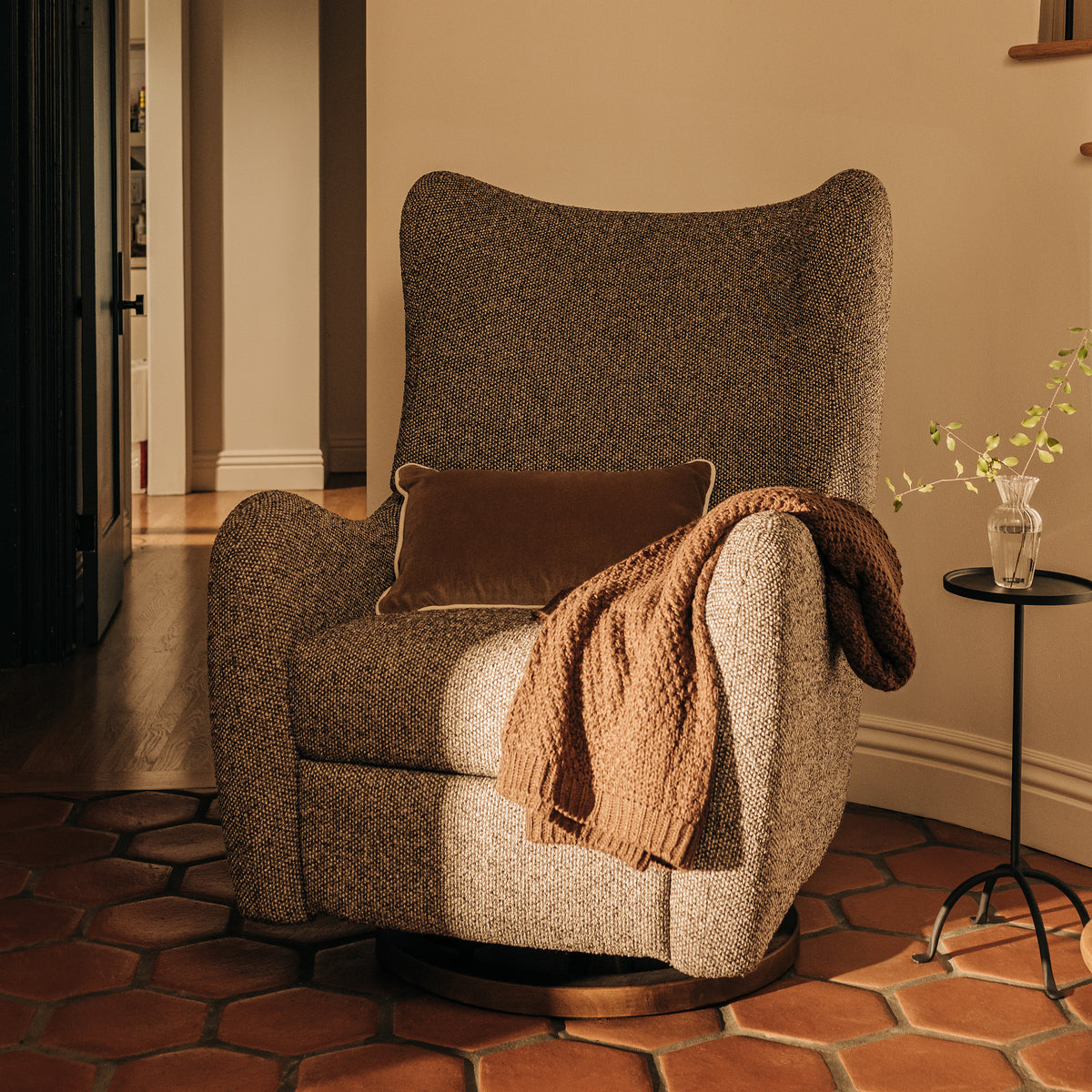 Babyletto textured brown wingback swivel glider chair with a throw blanket and pillow