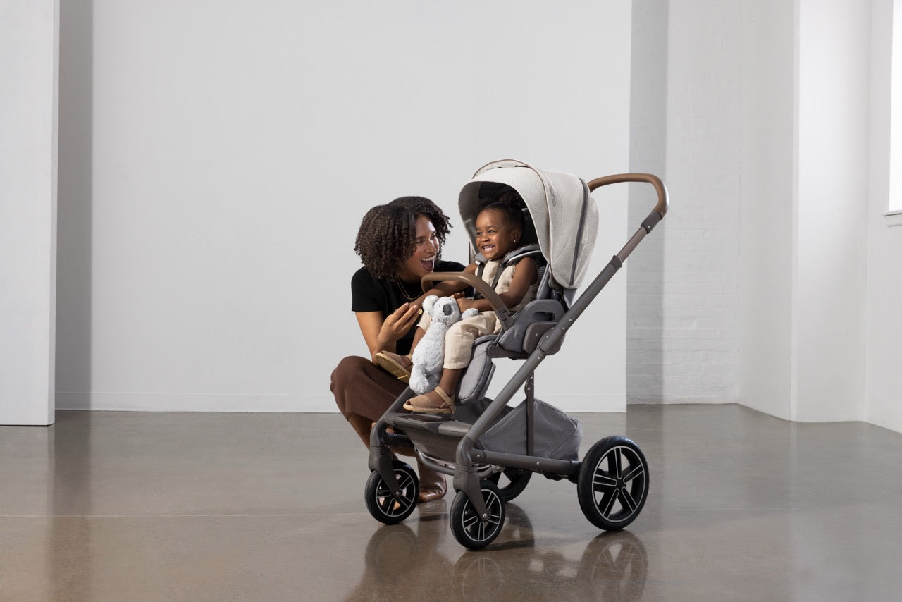 Woman crouching next to a child sitting in a Nuna stroller