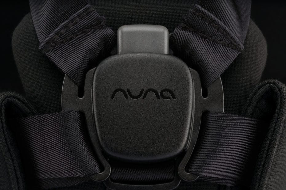 Close-up of black Nuna car seat buckle with textured straps, embossed logo, and dark fabric background.
