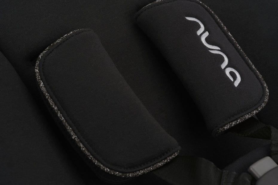 Close-up of black Nuna car seat straps with white logo, textured edges, and soft padding.