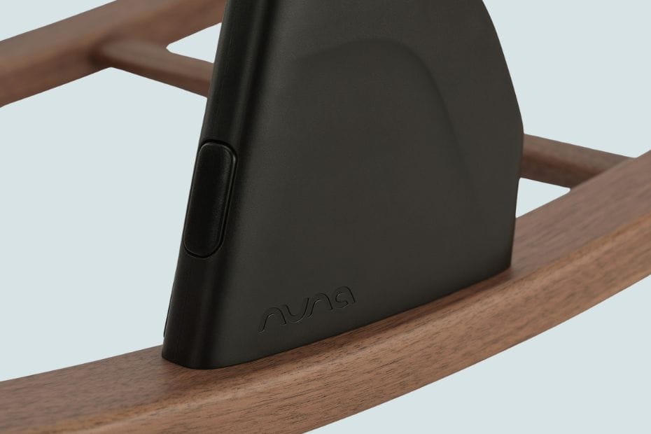 Black Nuna device with embossed logo rests on warm-toned wooden frame, soft lighting.