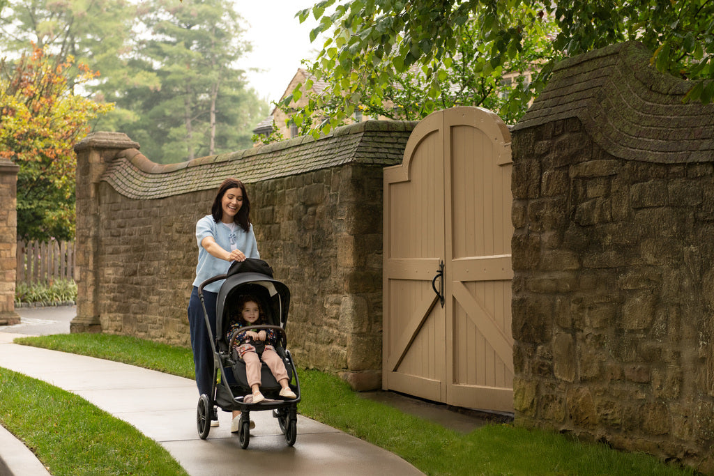 Woman pushing a child in a black stroller along a stone wall path