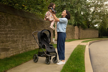 Woman lifting a toddler near a Nuna stroller on a sidewalk