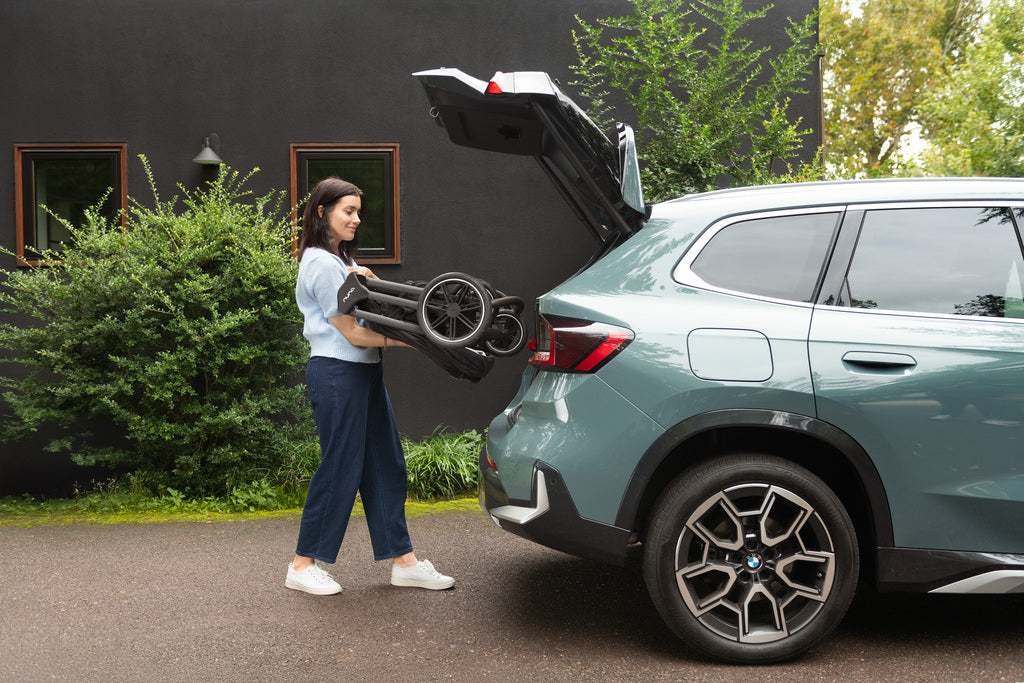 Woman loading a folded Nuna stroller into the trunk of a car