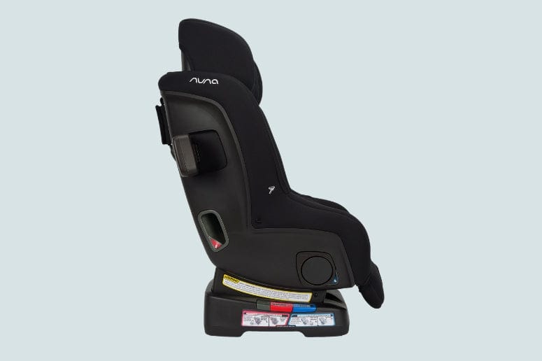 Side view of a black Nuna brand car seat with headrest and base, against a pale blue background.