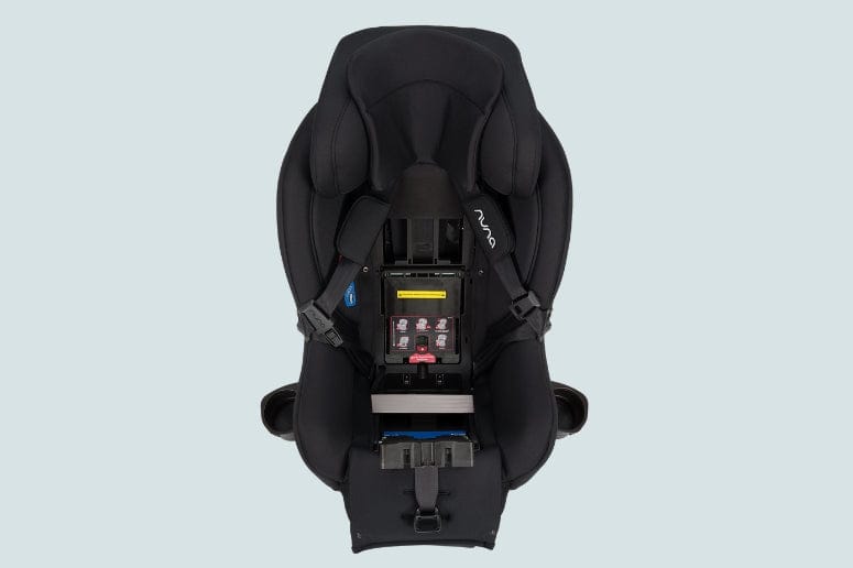 Overhead shot of a black Nuna car seat, showing the internal mechanisms, harness, and safety labels on a light blue background.