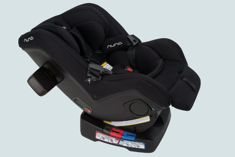 A black Nuna brand infant car seat is on a black base against a light blue background.