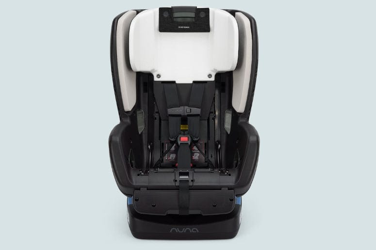A black and white Nuna brand car seat faces forward, featuring harness straps and adjustment mechanisms. The background is plain light blue.
