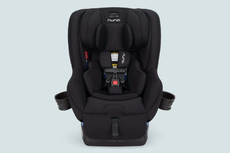 A black Nuna EXEC car seat faces forward on a light blue background. It features head and body support, a five-point harness, and two cup holders. The Nuna logo is visible.