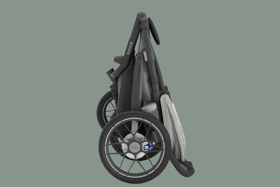 Folded black RUGG stroller with large front wheel, grey canopy, and blue brake, on muted green background.