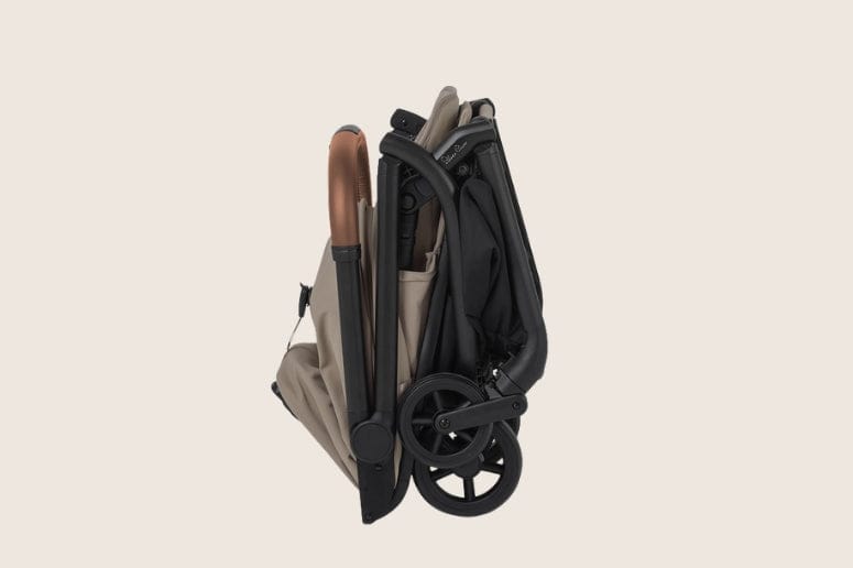 A folded Silver Cross Dune stroller stands upright, with a beige seat and brown handle on the left, and black frame and wheels on the right.