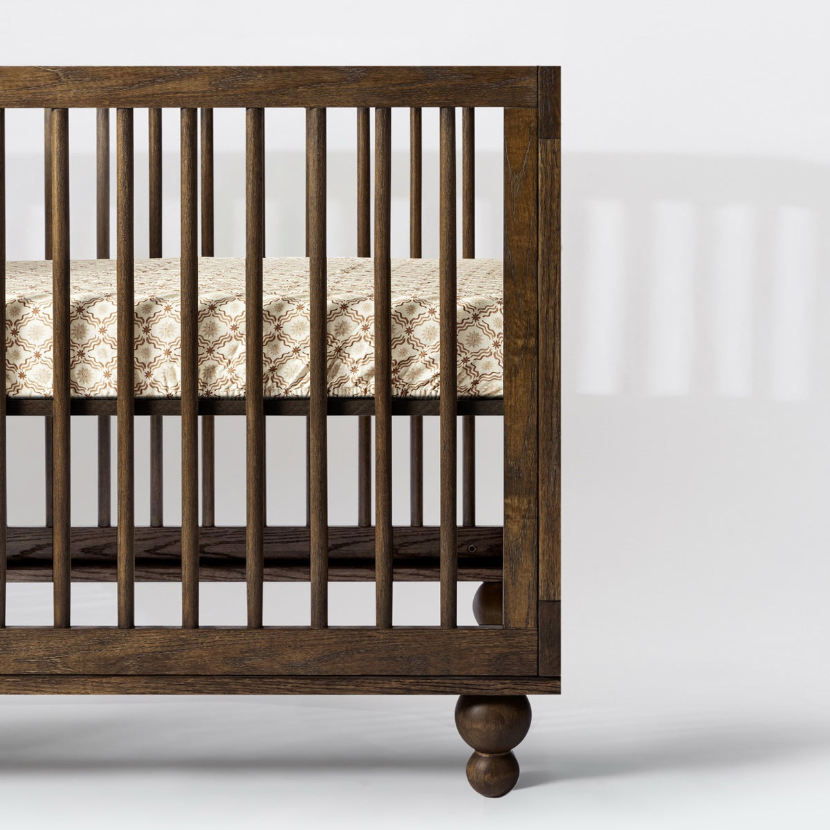 Babyletto dark wood crib with spindle sides and patterned mattress sheet