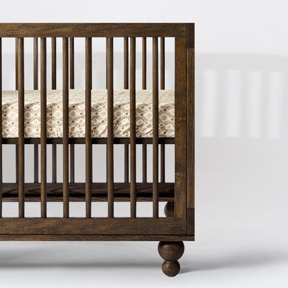 Babyletto dark wood crib with spindle sides and patterned mattress sheet