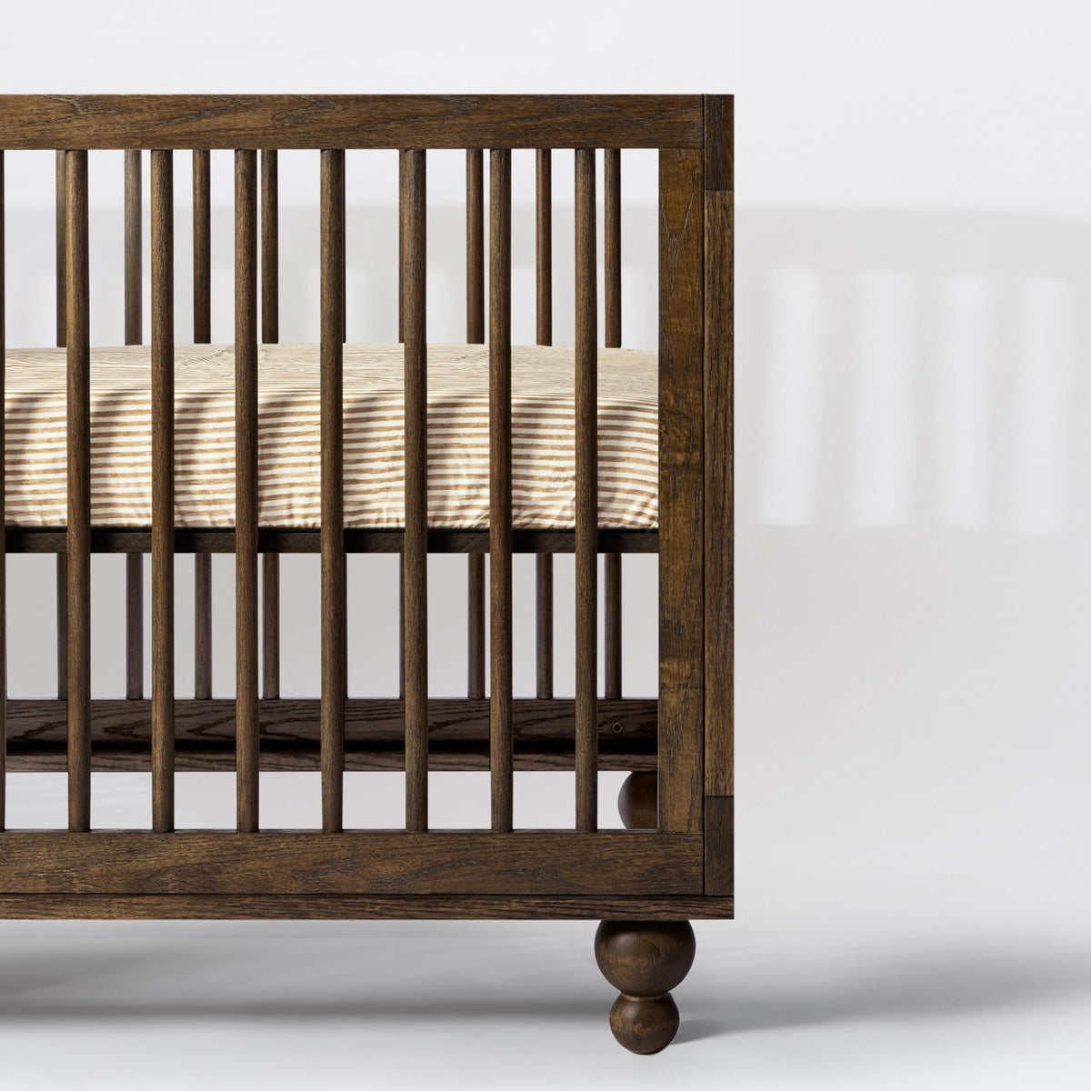 Babyletto dark wood crib with vertical slats and striped mattress