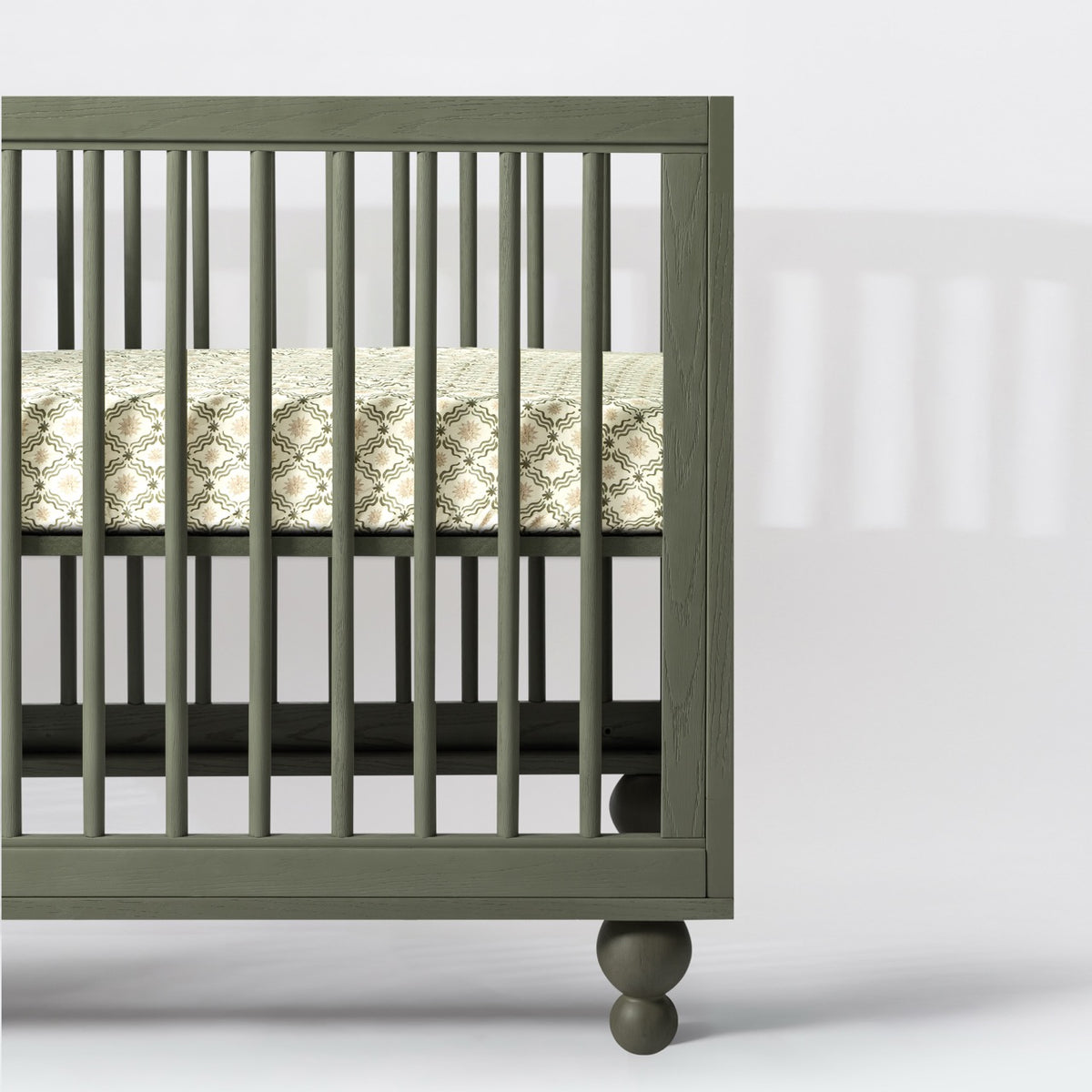 Babyletto olive green wooden crib with spindle slats and patterned mattress