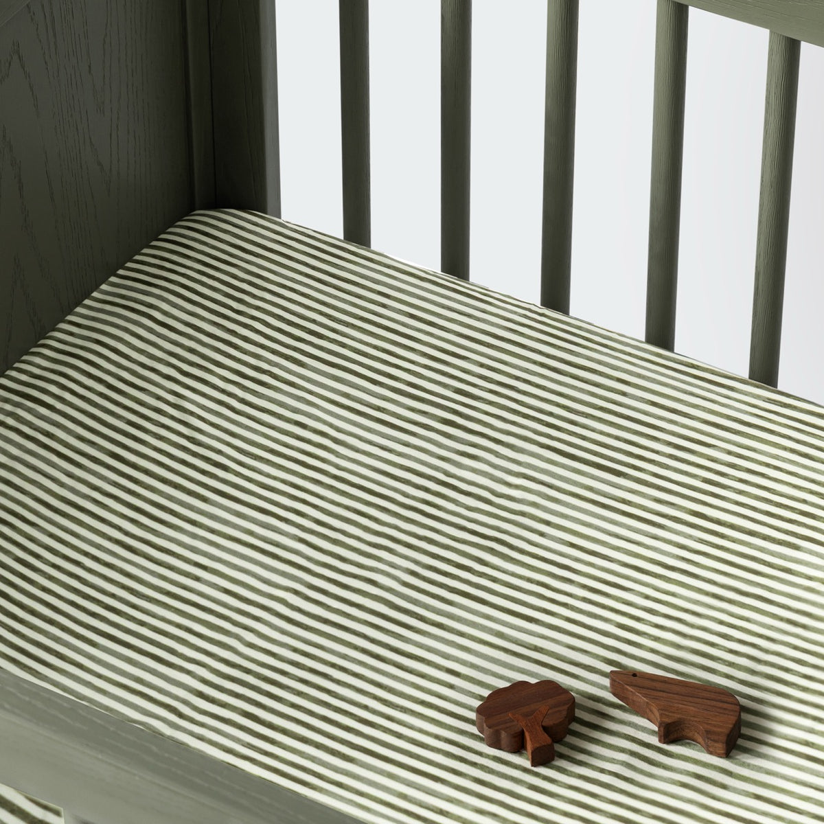 Babyletto crib mattress with green and white striped sheet and two small wooden animal figures