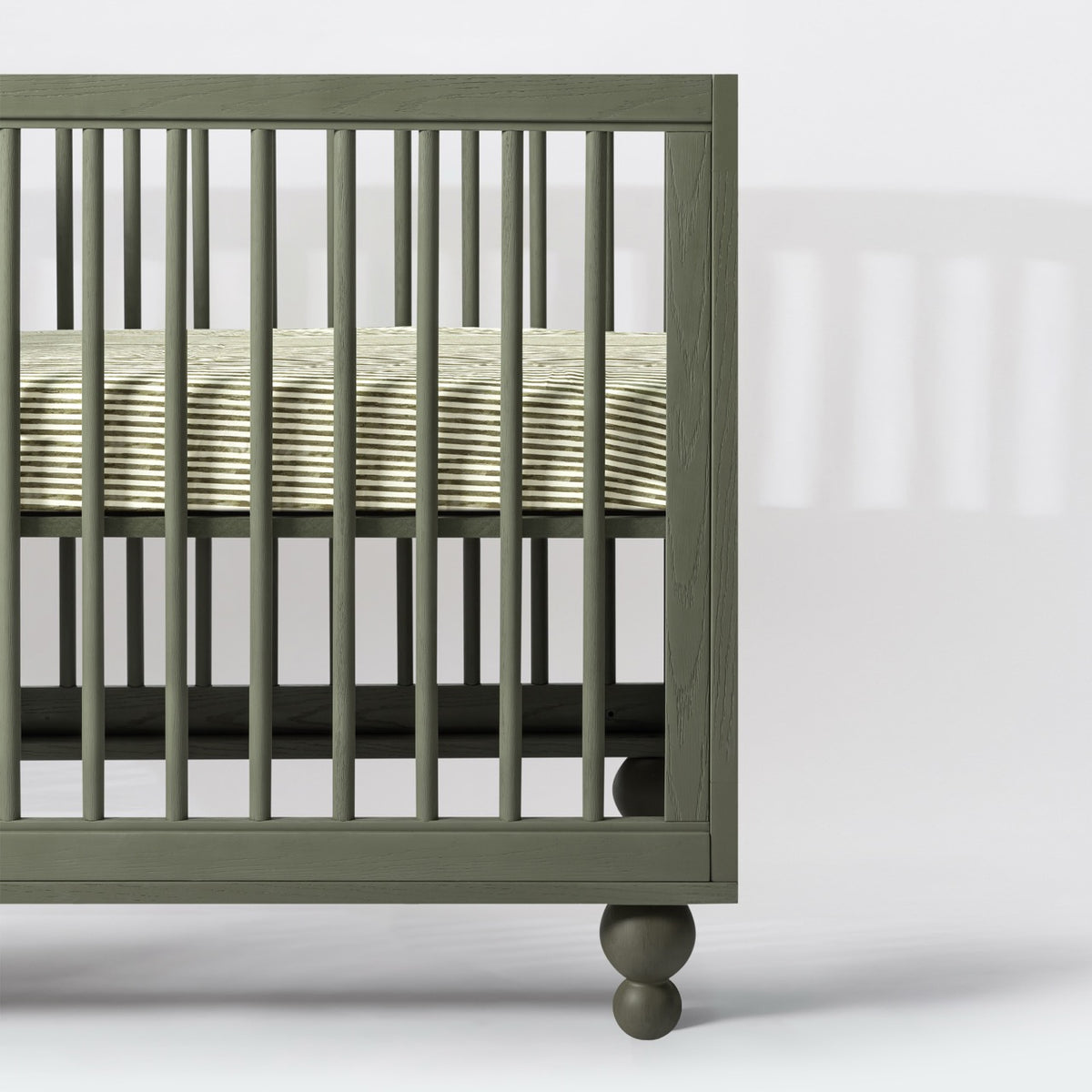 Babyletto olive green wooden crib with spindle slats and striped mattress