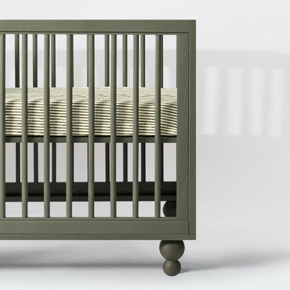 Babyletto olive green wooden crib with spindle slats and striped mattress