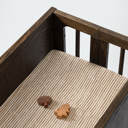 Babyletto crib with striped sheet and two wooden tree toys