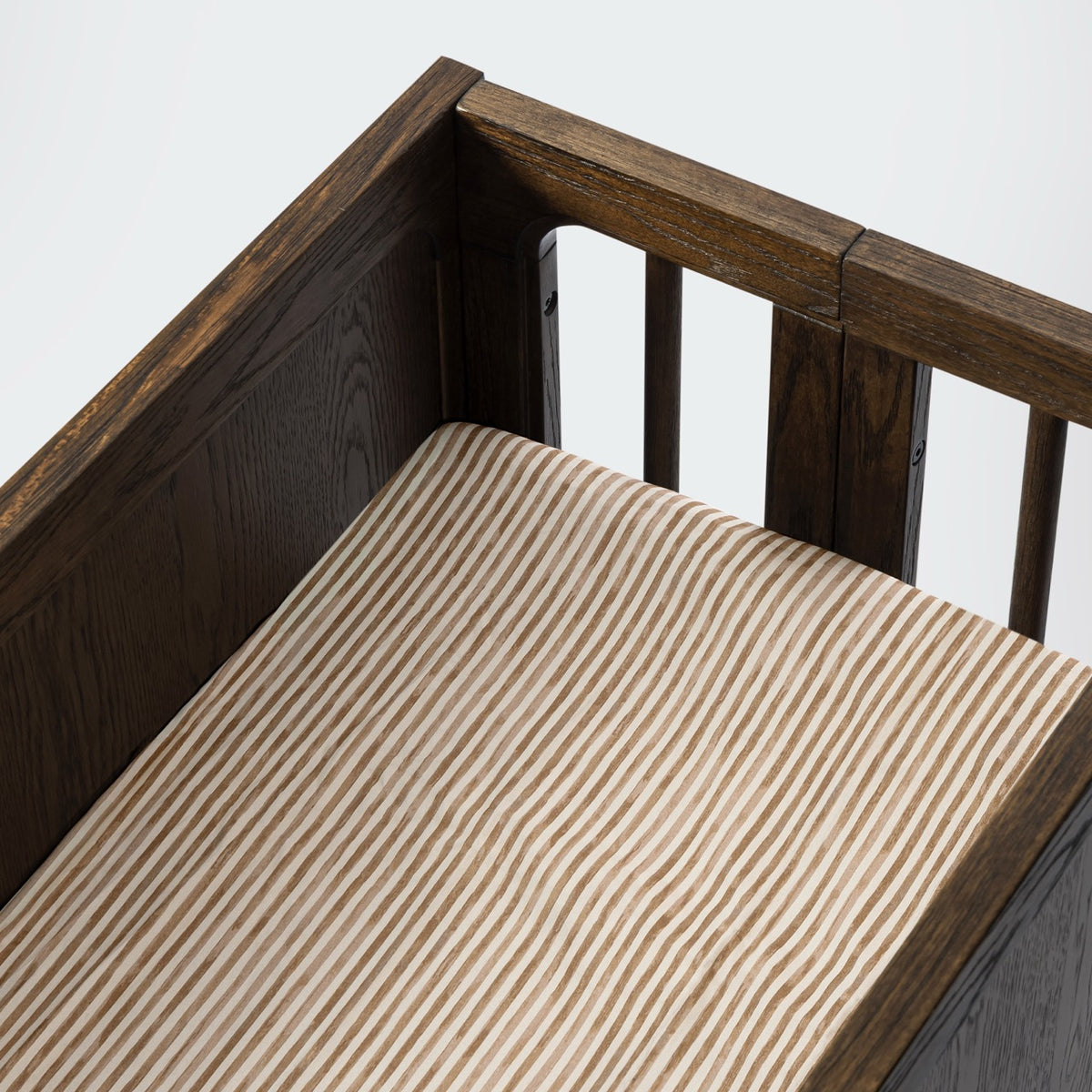 Babyletto crib with dark wood frame and beige striped mattress sheet