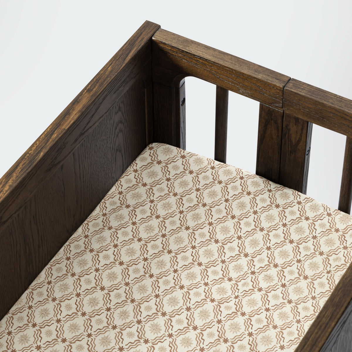 Babyletto crib with a patterned sheet featuring brown star and wave motifs on a cream background