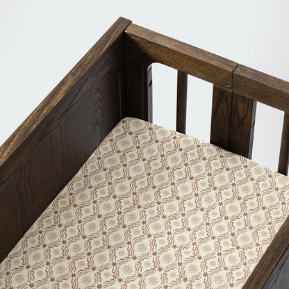 Babyletto crib with a patterned sheet featuring brown star and wave motifs on a cream background