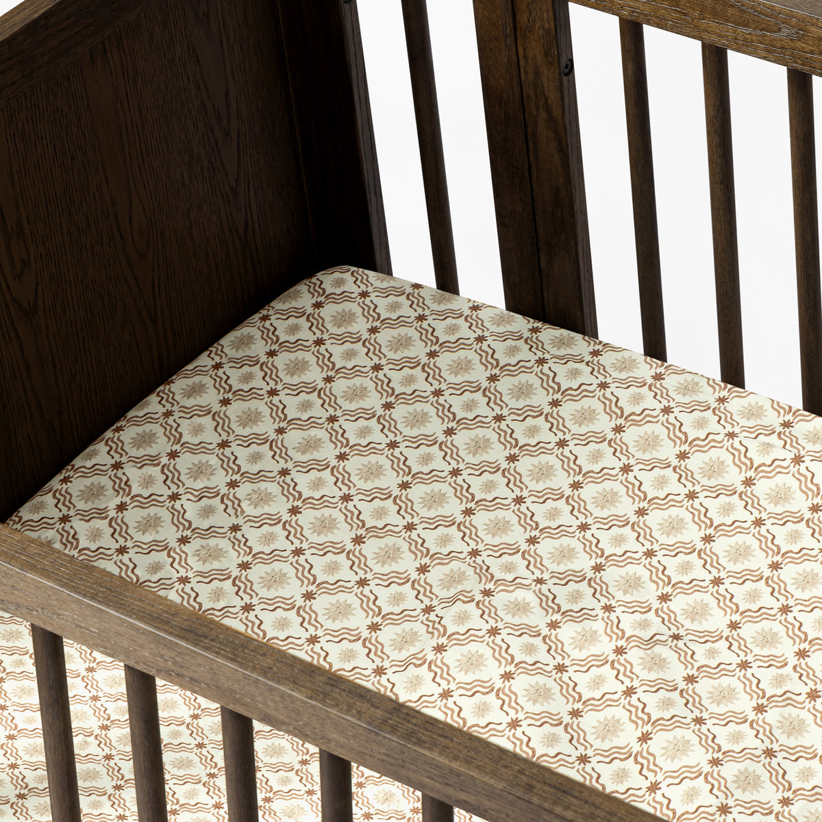 Babyletto crib with patterned mattress sheet featuring brown star and wave design