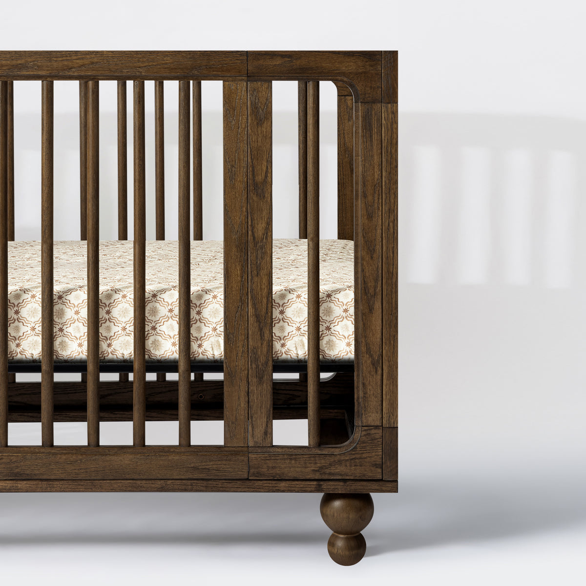 Babyletto dark wood crib with spindle sides and patterned mattress