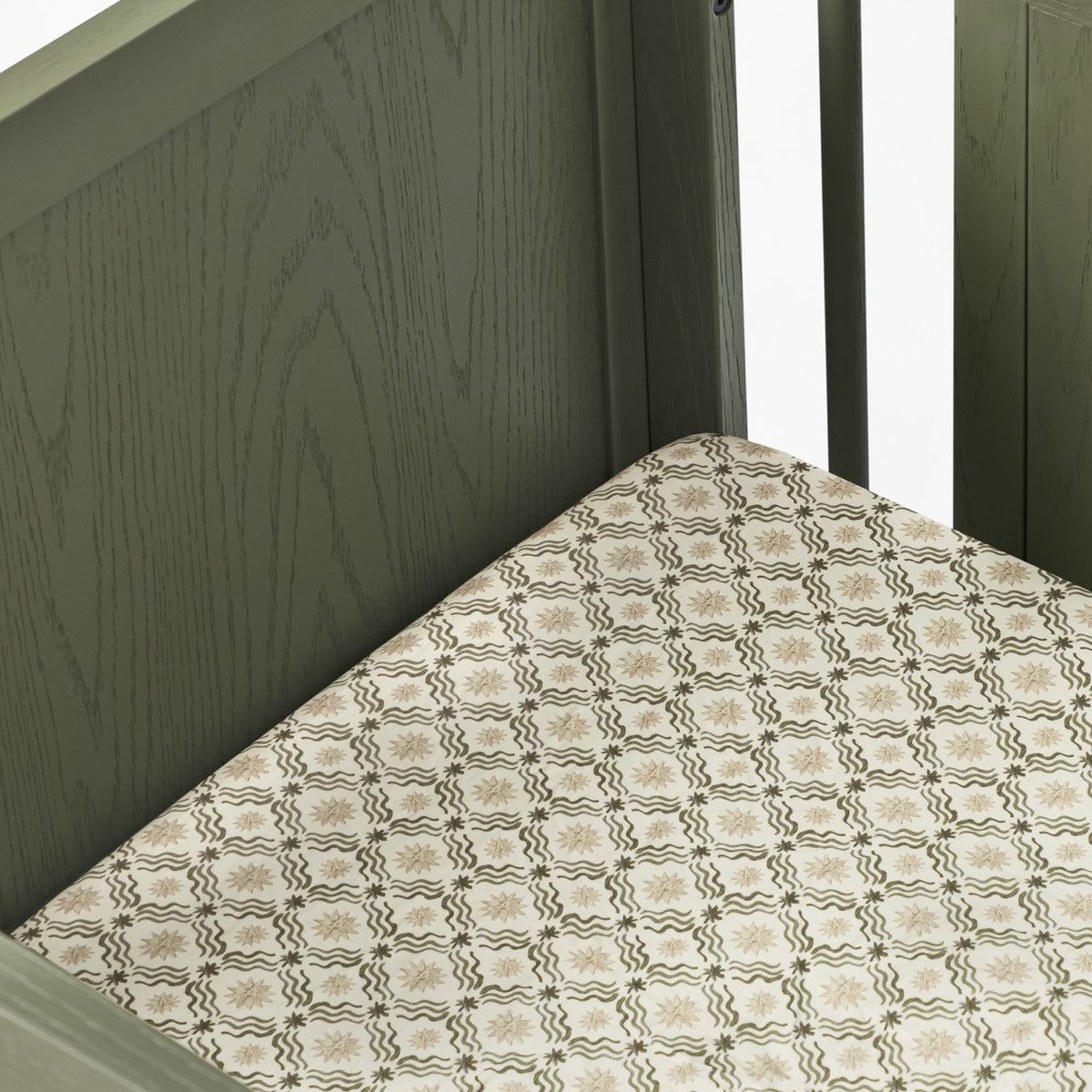 Babyletto crib with olive green wooden frame and patterned mattress sheet
