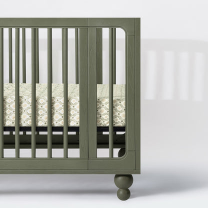 Babyletto olive green wooden crib with patterned mattress sheet