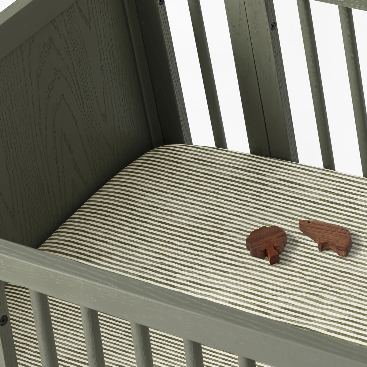 Babyletto crib with striped mattress sheet and two small wooden animal figures