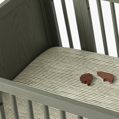 Babyletto crib with striped mattress sheet and two small wooden animal figures