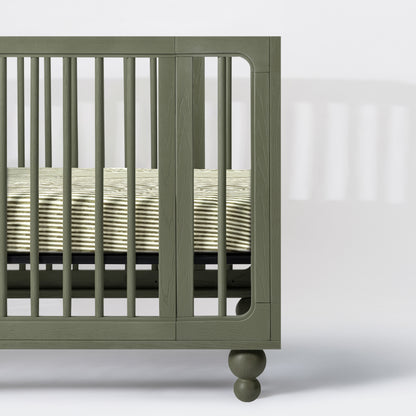 Babyletto olive green wooden crib side view with striped mattress sheet