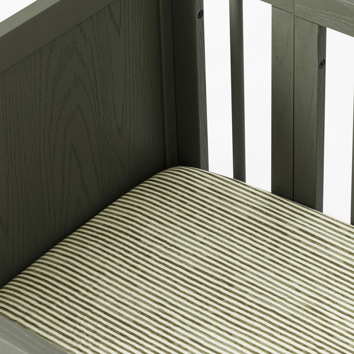 Close up of Babyletto crib corner with dark wood frame and striped mattress