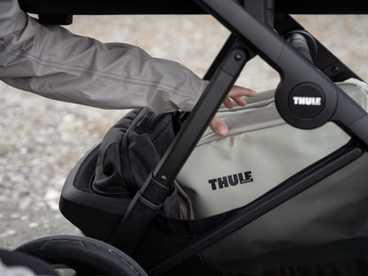 Person placing a Thule bag into the storage basket of a Thule stroller