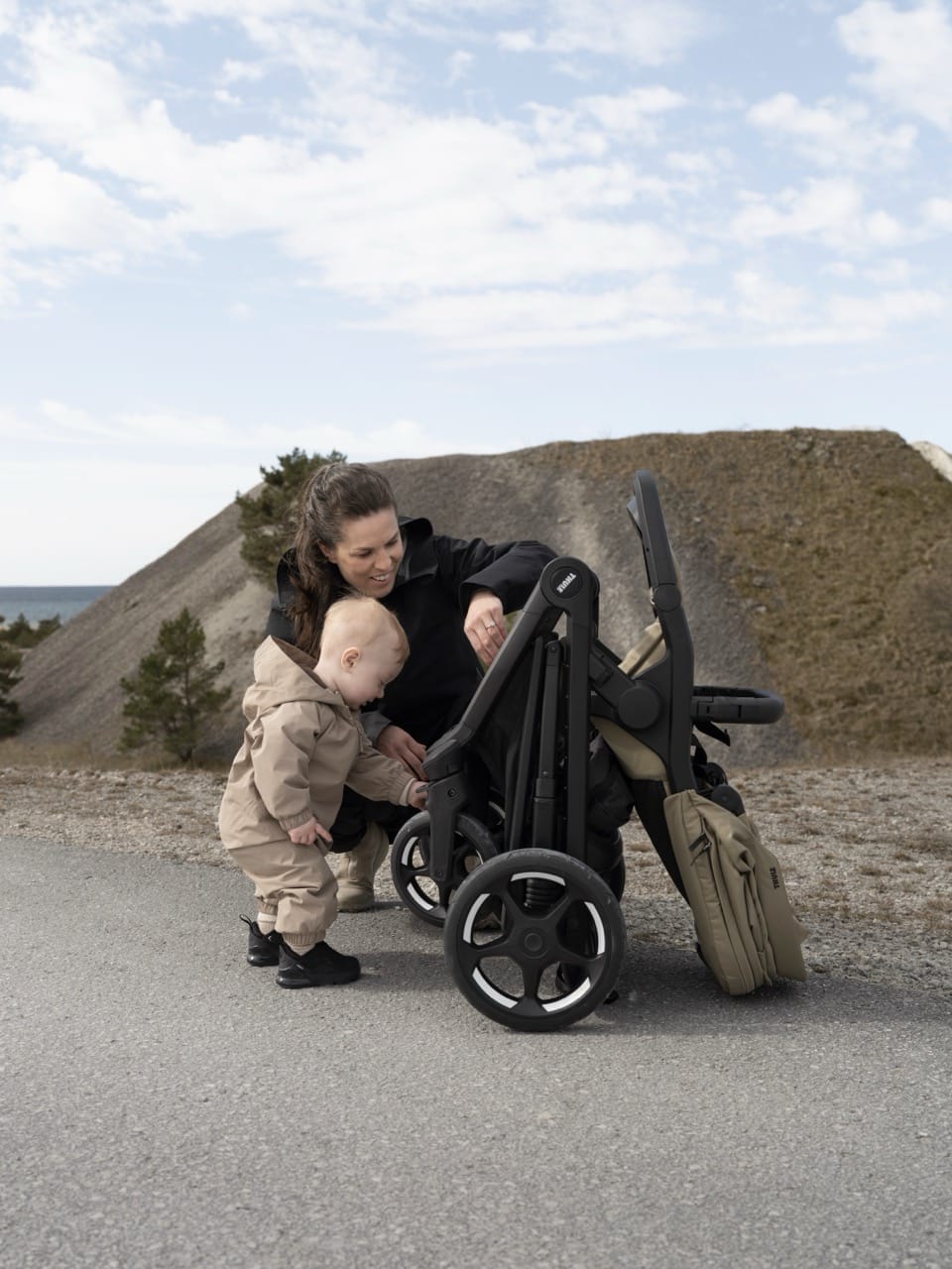 Woman and toddler standing next to a folded Thule stroller on a paved path