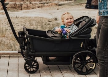 Toddler sitting in a black Veer cruiser wagon on a wooden boardwalk