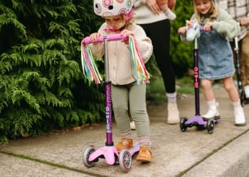 Child riding a purple Micro scooter with colorful handlebar streamers