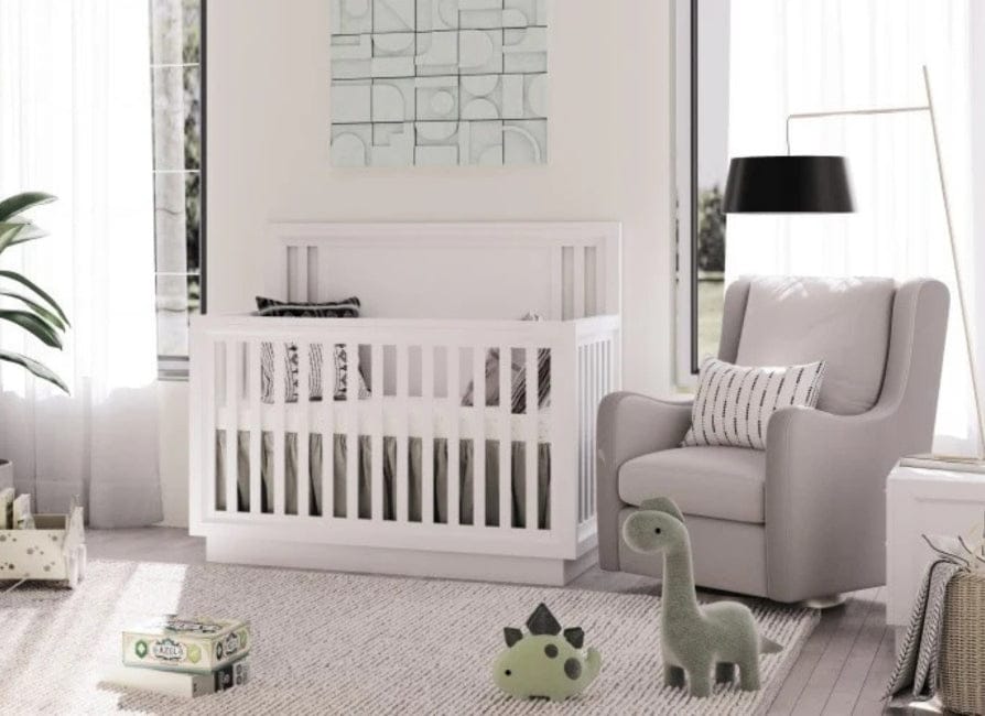 White crib with gray and white bedding in bright nursery, gray armchair, green dinosaur toys, and abstract wall art.