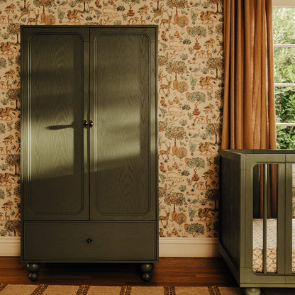 Babyletto olive green wooden wardrobe with two doors and a bottom drawer against patterned wallpaper