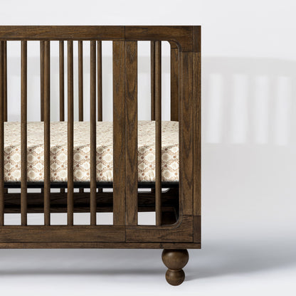 Babyletto dark wood crib with spindle sides and patterned mattress