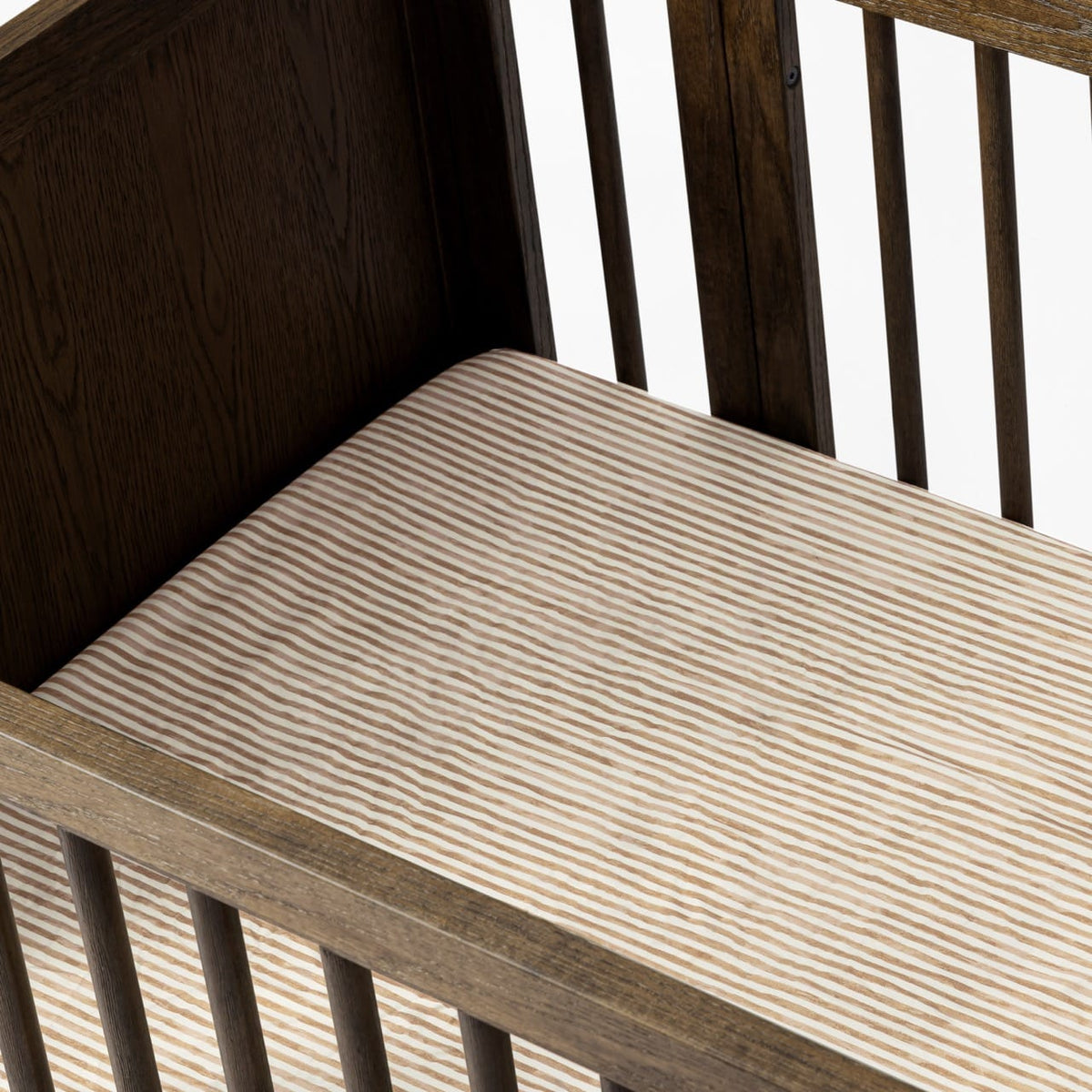 Babyletto crib with brown and white striped mattress sheet