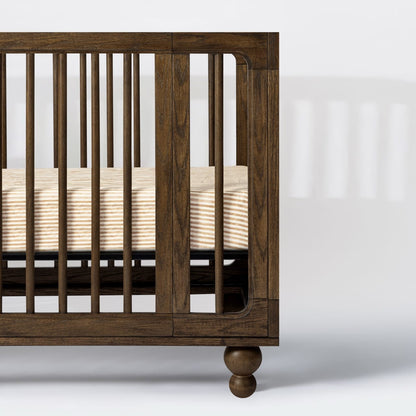 Babyletto dark wood crib with spindle sides and striped mattress