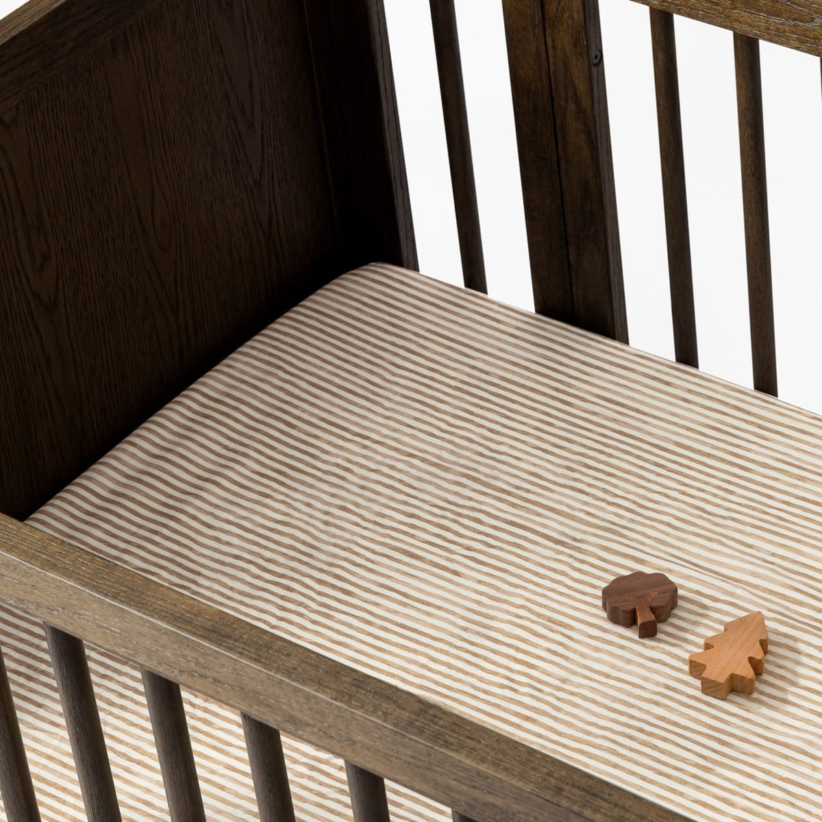 Babyletto crib with striped sheet and two wooden tree toys