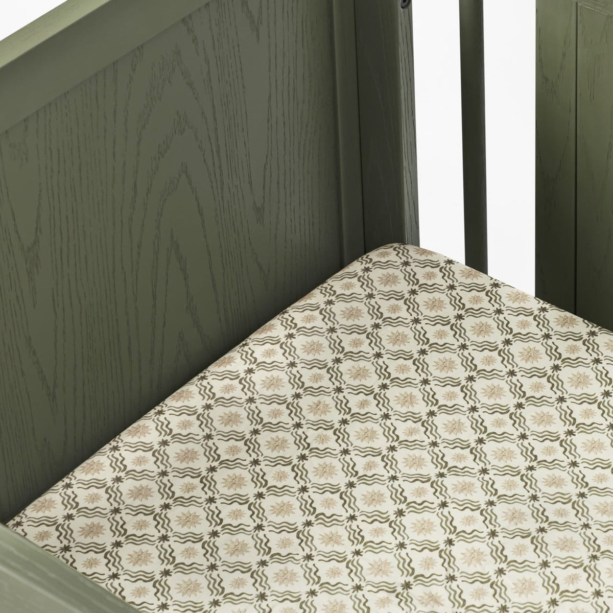 Babyletto crib with olive green wooden frame and patterned mattress sheet